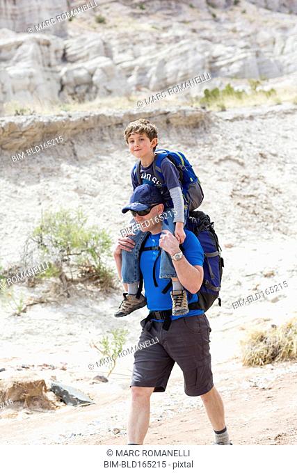 Caucasian father carrying son on shoulders on dirt path