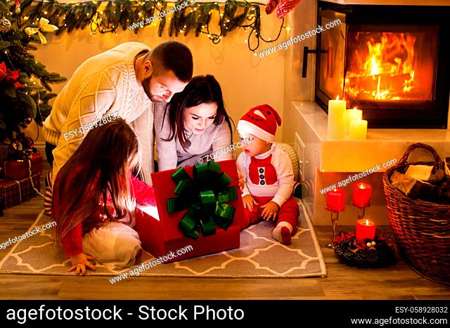 Happy family open Christmas lighting gift box near Christmas tree. Family celebrate Christmas in magic night