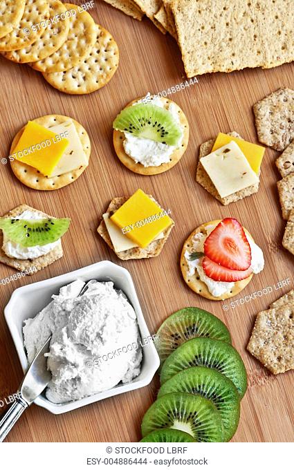 Assorted crackers on a cutting board with cream cheese, cheddar cheese kiwi and strawberry