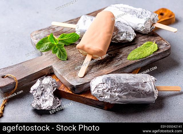 Artisanal ice cream in chocolate glaze on a wooden serving board, selective focus. Textured gray background