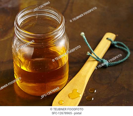 A jar of honey and a drips of honey on a wooden spoon