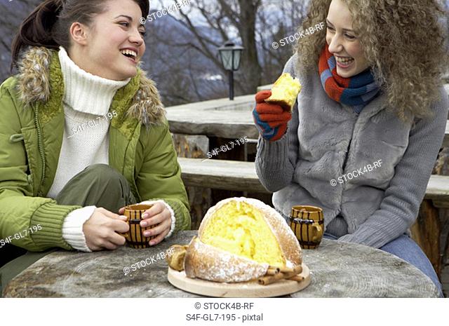 Three friends having hot beverage and cake in a winterly landscape
