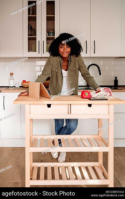 Smiling woman with tablet PC and mesh bag on kitchen island at home