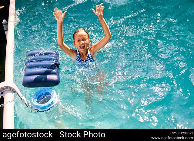 Happy little girl having fun in the swimming pool, dives and swim, summer vacation at home, tropical holiday resort