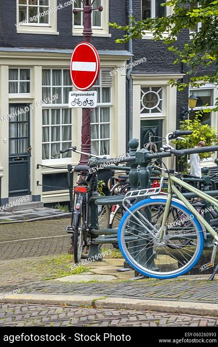 Netherlands. Amsterdam canal promenade with traditional houses and parked bicycles. Under the prohibition sign there is a sign in Dutch ""except for""