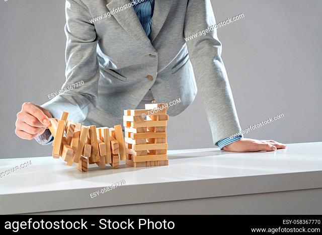 Businesswoman removing wooden block from falling tower on table. Management of risks and economic instability concept with wooden jenga game