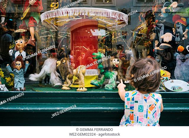 Czechia, Prague, back view of little girl standing in front of toy shop looking at puppets