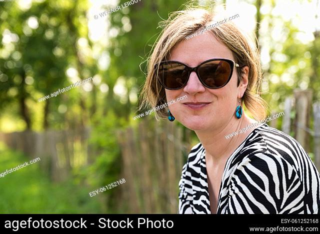 Smiling white 30 yo woman wit sunglaas in a park, Uccle, Brussels, Belgium