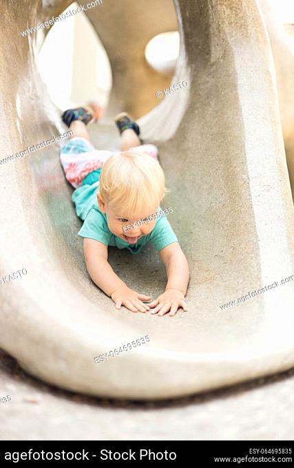 Child playing on outdoor playground. Toddler plays on school or kindergarten yard. Active kid on stone sculpured slide. Healthy summer activity for children