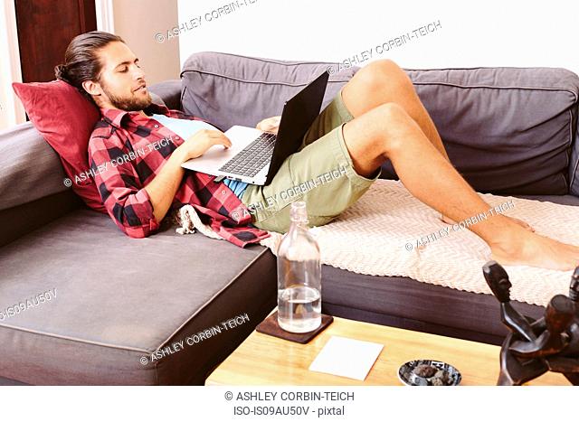 Young man relaxing on sofa, using laptop