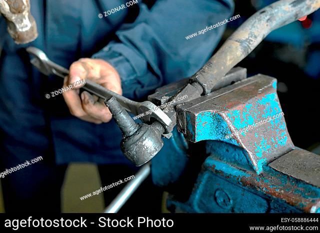 A car mechanic repairs a part of the car. An employee of an auto repair shop has clamped the steering rod in a vise and is repairing it. Close-up