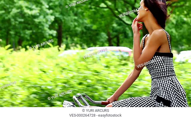 Gorgeous young woman smiling at you while cycling along a country road under trees on a summer day