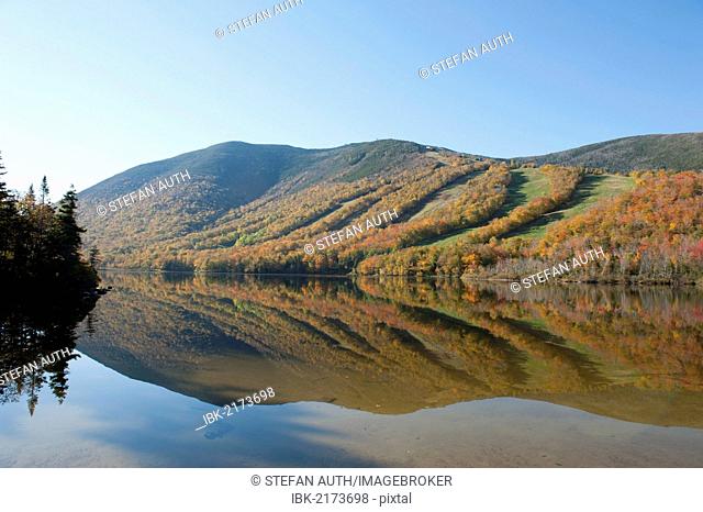 Ski slopes in autumn reflected in Profile Lake, foliage coloured during Indian Summer, Franconia Notch State Park, White Mountains National Forest