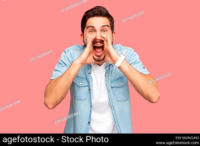 Portrait of crazy handsome bearded young man in blue casual style shirt standing with hand on face, looking at camera and screaming