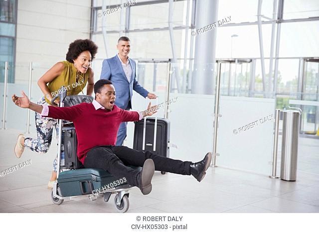 Playful couple running with luggage cart in airport