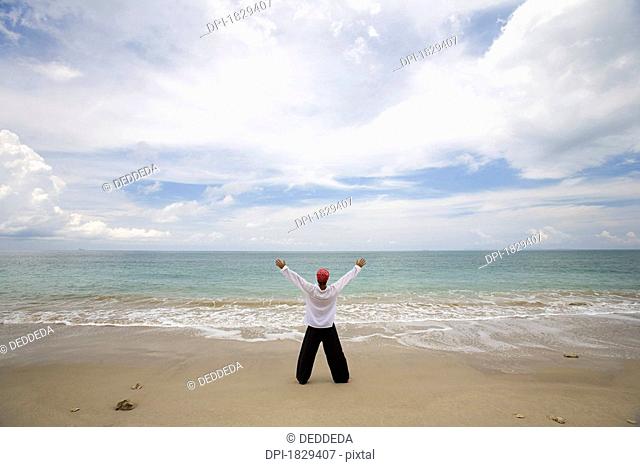A man with arms outstretched on a beach in Koh Lanta, Thailand