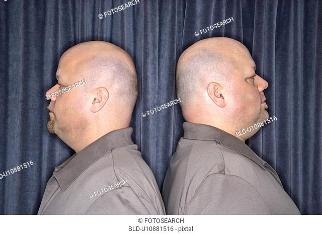Profile of bald identical twin mid adult men standing back to back