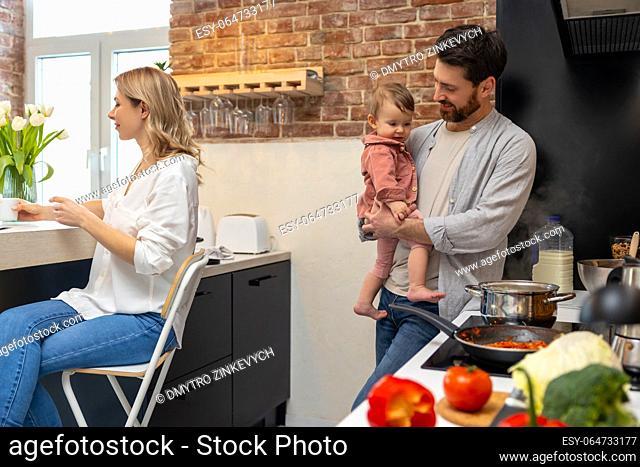 Happy family at home in the kitchenn man with baby cooking making meal woman sitting at table