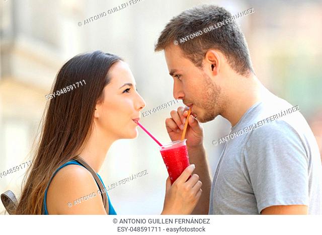 Side view portrait of a happy couple sipping a slush together outdoors in the street