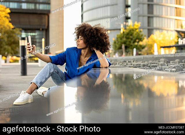 Afro woman taking selfie through mobile phone leaning on wall