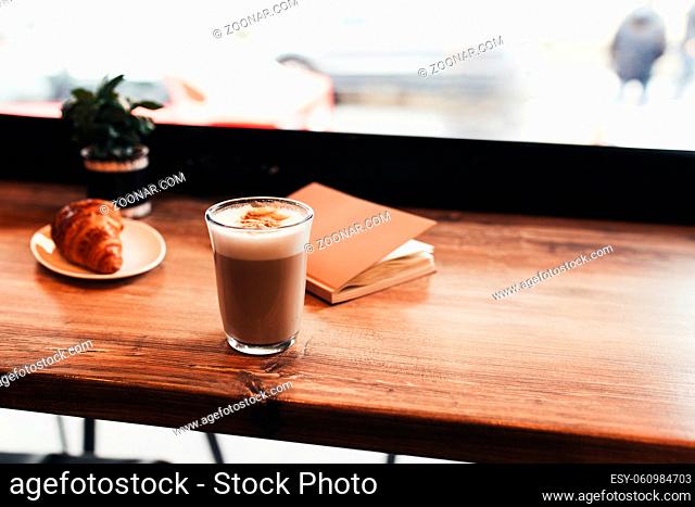 Cup of coffee, croissant, notebook at table in cafe. Blurred background. High quality photo