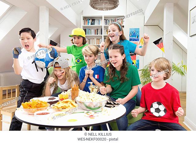 Group of kids watching soccer world championship with table full of sweets and snacks