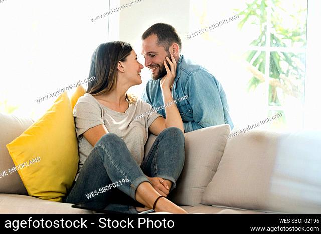 Affectionate couple in love about to kiss while relaxing at home on couch