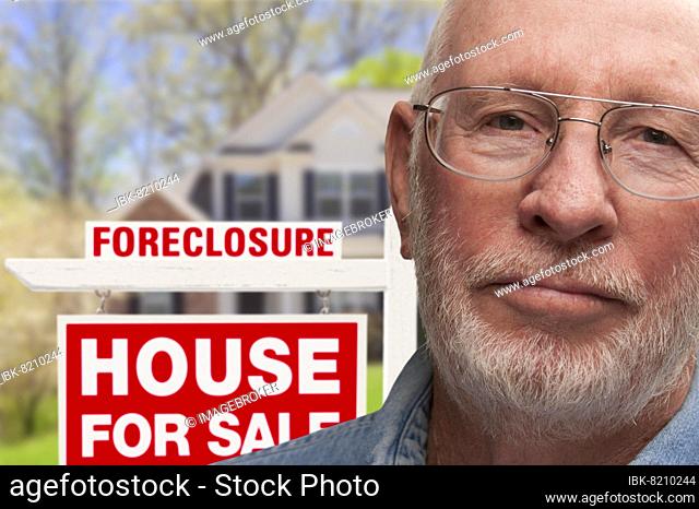 Depressed senior man in front of foreclosure real estate sign and house