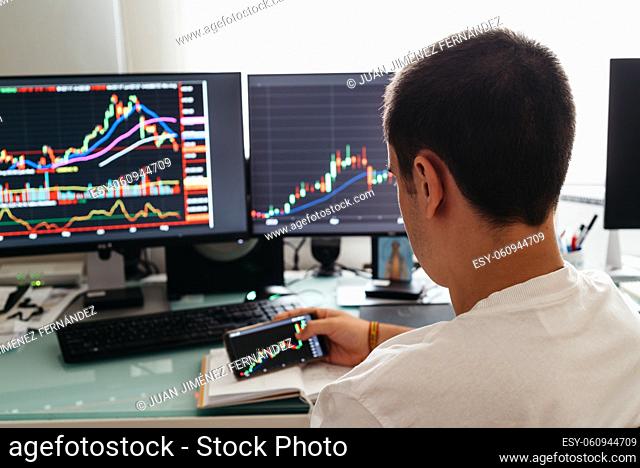 Busy working day at home. Side view of successful young trader in casual wear working with charts and market reports on computer screens in his home
