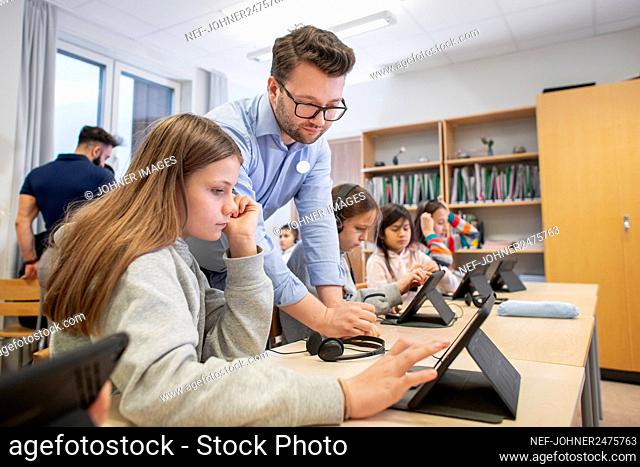 Teacher helping schoolgirl in classroom