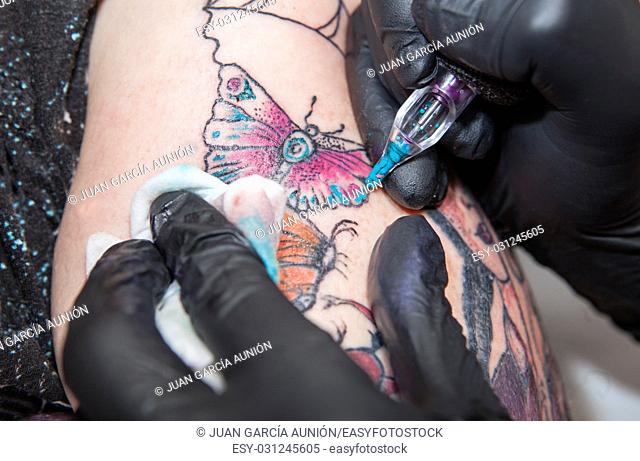 Tattoo artist applies tattoo to arm. She is filling with light blue color the tattoo