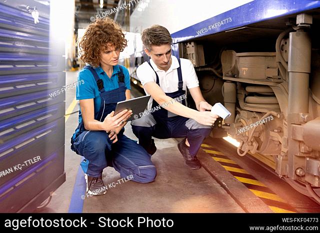 Engineer holding tablet PC sitting by trainee analyzing monorail with thermal scanner in factory
