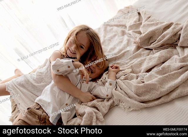 Portrait of little girl cuddling her laughing brother on bed