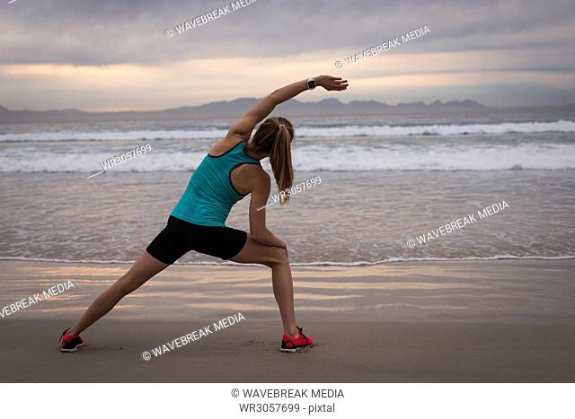 Woman performing stretching exercise on the beach during sunset