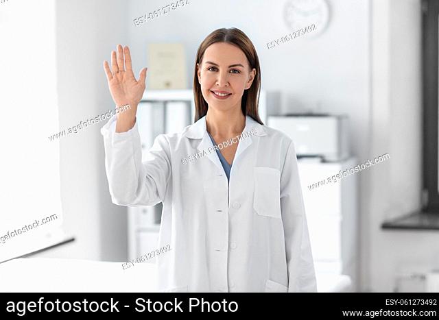 smiling female doctor waving hand at hospital