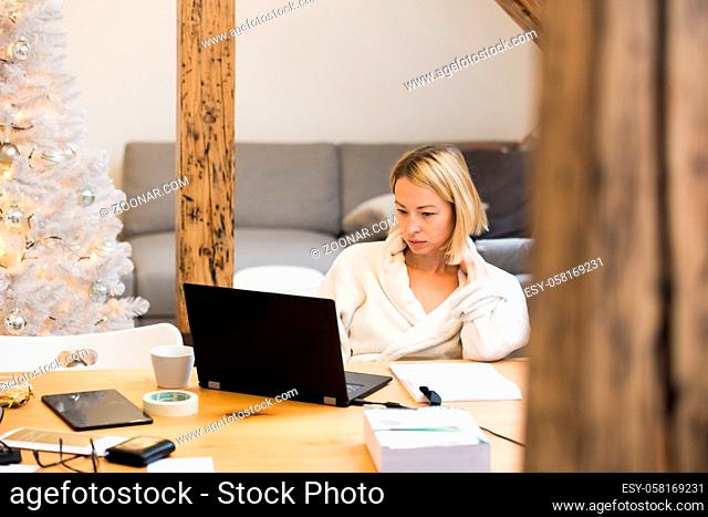 Young businesswoman wearing cosy warm bathrobe working remotly from home in winter Christmas time during 2020 corona virus pandemic