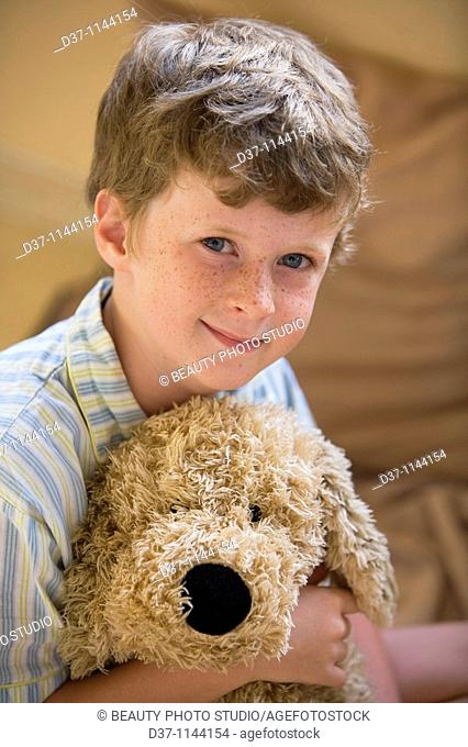 Fair-haired boy in bed hugging a cuddly toy