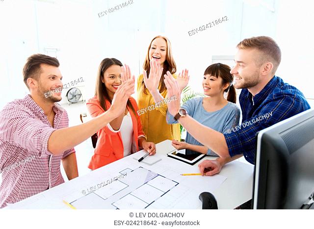 business, startup, architecture, gesture and people concept - happy international creative architect team or students with blueprint making high five at office