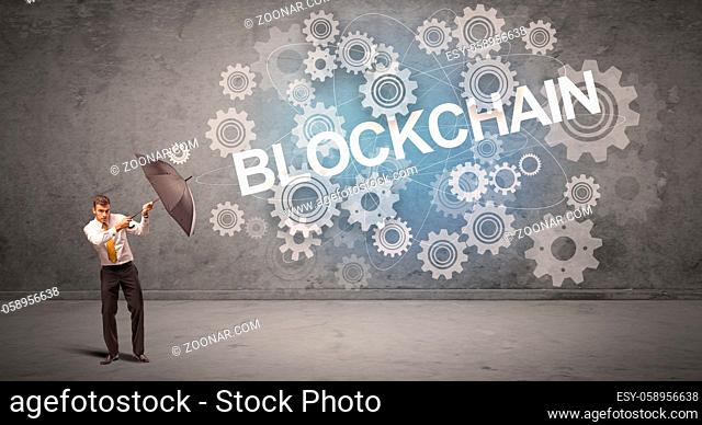 Businessman defending with umbrella from BLOCKCHAIN inscription, technology concept