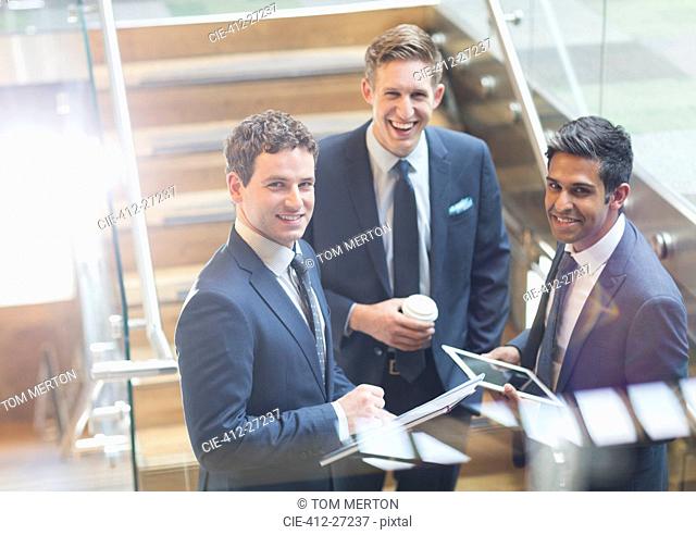 Portrait confident businessmen with coffee and digital tablet on stairs