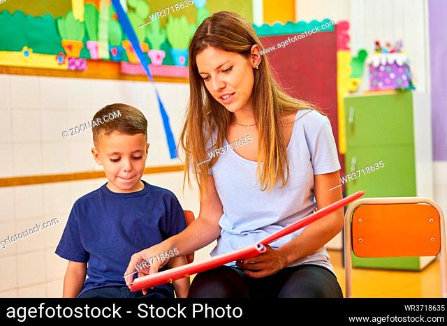 Erzieherin oder Tagesmutter mit Kind beim Buch vorlesen im Kindergarten oder Hort