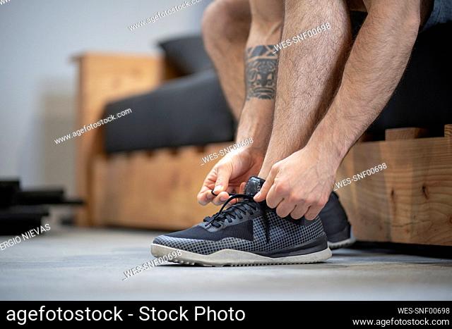 Close-up of man tying shoelace while sitting on bed at home