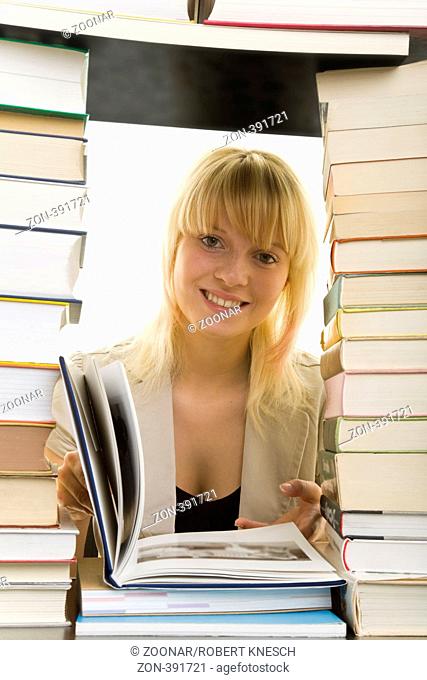 Junge Frau schaut lachend durch einen großen Bücherstapel