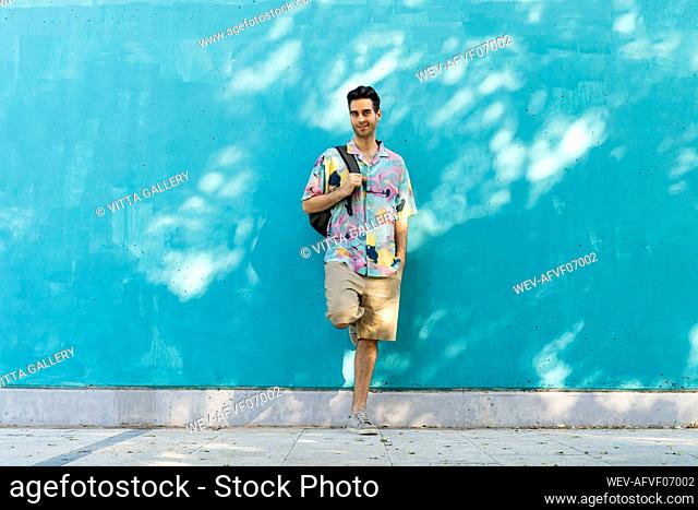 Casual man leaning against blue wall