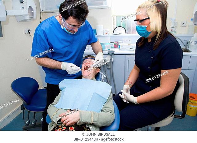 Dentist carrying out dental treatment on a patient, while dental nurse looks on