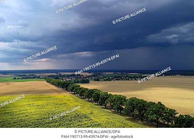 13 July 2019, Brandenburg, Petersdorf: Thunderstorm clouds are moving over the landscape with a field of sunflowers in the Oder-Spree district (aerial...