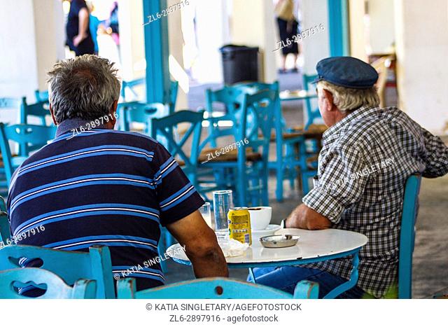 Street life scene of two caucasian gentlemen in their mid 50's sitting at an outdoor cafe smoking a cigarette and enjoying their drink, in Oia, Santorini