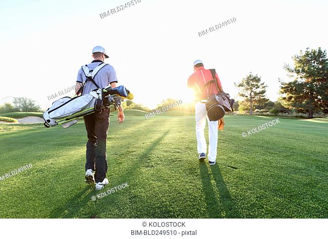 Men carrying golf bags on sunny golf course