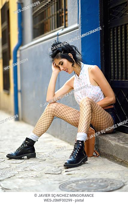 Fashionable woman sitting on step in front of house entrance