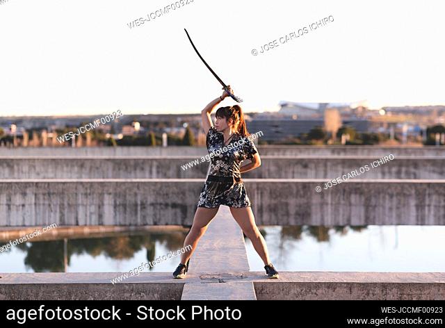 Young female sportsperson practicing sword on structure against clear sky at sunset